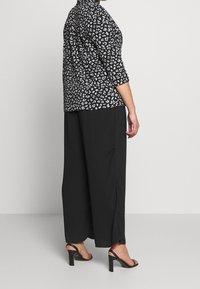 Blouse à imprimé léopard noir et blanc avec manches trois-quarts, associée à un pantalon noir à jambes larges et des talons noirs. Texture de tissu lisse.