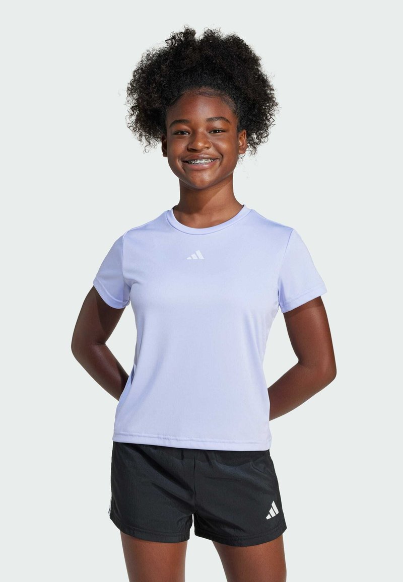 Camiseta deportiva de color lila con mangas cortas y cuello redondo, que presenta un logo blanco en el pecho, combinada con pantalones cortos negros.