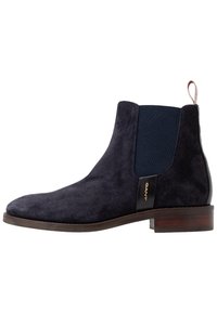 Maritieme suède Chelsea-boots met elastische zijpanelen, een bruine houten hak en een gouden logo-detail aan de zijkant. Gladde textuur, slank ontwerp.