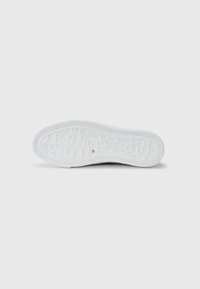 Suola di sneaker bianca in gomma testurizzata; presenta branding in rilievo. Forma leggermente curvata con suola piatta e design pulito.