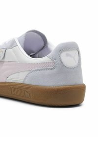 Sneaker bianco e grigio chiaro con un accento in suede, suola in gomma, dettagli cuciti e logo Puma sul tallone. Materiali lisci e texturizzati.