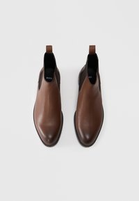 Bottines Chelsea en cuir marron avec une finition texturée, bout pointu, panneaux latéraux élastiques et languettes au talon pour un enfilage facile. Logo BOSS visible à l'intérieur.