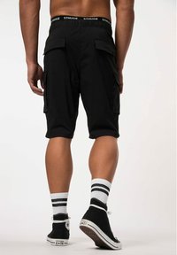 Pantalones cortos de cargo negros con una cintura ajustable, que cuentan con bolsillos laterales y un corte relajado, combinados con zapatillas negras y calcetines rayados blancos.