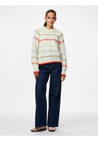 Adīta krēmsvārna ar horizontālām daudzkrāsainām svītrām sarkanā, rozā un zilā krāsā. Kombinēta ar tumši ziliem platiem džinsiem un gaišām apaviem.