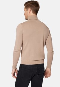 Beżowy sweter w półgolf z prążkowanym wzorem, z długimi rękawami i dopasowanym krojem, w zestawieniu z ciemnymi dżinsami.