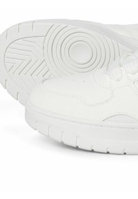 Weiße Sportschuhe mit einer strukturierten Gummisohle, die über kreisförmige und Zickzack-Muster verfügt, sowie einem genähten Leder-Obermaterial mit Schnürsenkeln.