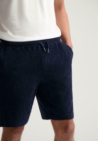 Navy blue patterned shorts made of textured fabric, featuring an elastic waistband with a drawstring and two side pockets.