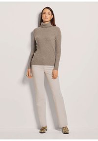 Hellgrauer gerippter Rollkragenpullover mit Slim-Fit, kombiniert mit beigen geraden Hosen und gemusterten Schuhen, vor einem neutralen Hintergrund.