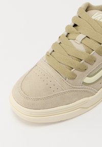Pointe de basket en daim beige avec des lacets vert olive, des détails perforés et une semelle en caoutchouc crème sur fond blanc.