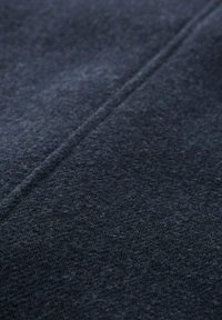 Tela de lana azul oscuro con una superficie difusa y texturizada y una costura visible que atraviesa el marco en diagonal.