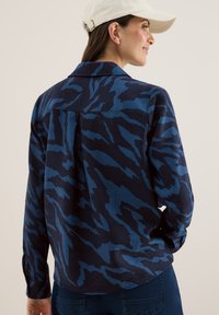 Camicia a collare in blu e navy con motivo, maniche lunghe e vestibilità rilassata, caratterizzata da un design astratto distintivo e un tessuto testurizzato.