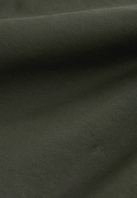 Tamnozeleni pamučni materijal s rebrastom teksturom, prikazuje mekane nabore i glatku površinu. Nema vidljivih uzoraka niti značajnih detalja.