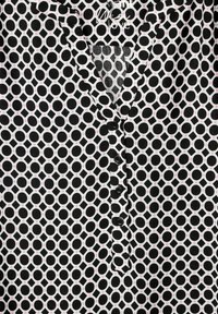 Blůza s černobílým vzorem, která obsahuje kruhové a diamantové tvary, s růžovými akcenty. Design s knoflíkovým zapínáním vpředu a límečkem. Měkká textura.