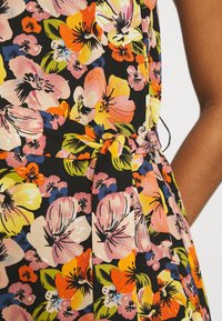 Vestido floral con fondo negro que presenta coloridas flores rosas, amarillas y naranjas, con cintura ajustada y diseño plisado. Textura de tela suave.