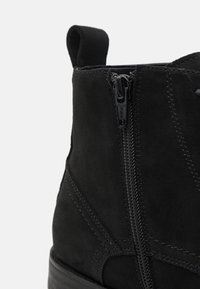 Bottine noire en daim doux avec une finition texturée, équipée d'une fermeture éclair latérale et d'une languette pour faciliter l'enfilage.