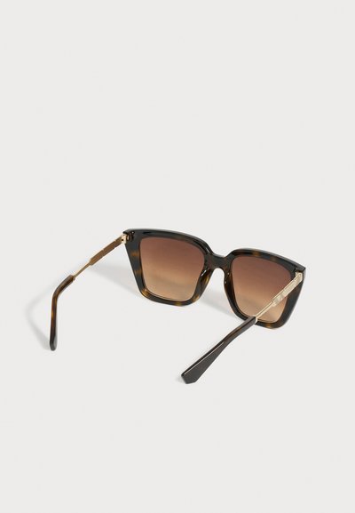 Lunettes de soleil carrées en écaille avec verres marron dégradés et branches en métal doré reposant sur une surface blanche.
