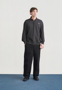 Μαύρο φούτερ με φερμουάρ και όρθιο γιακά, με μανσέτες με ριμπ, συνδυασμένο με άνετο μαύρο παντελόνι cargo που διαθέτει πολλαπλές τσέπες και υφή στην επιφάνεια.