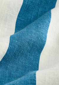 Gros plan sur un tissu texturé avec de larges rayures horizontales bleues et blanches, montrant le détail du tissage et des plis doux.
