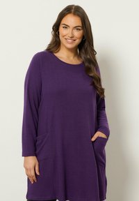 Tunika lunga viola con maniche lunghe realizzata in tessuto morbido e testurizzato. Presenta un collo rotondo e tasche laterali per praticità.