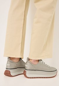 Sneaker platform grigie con tomaia testurizzata, lacci piatti e suola in gomma marrone. Abbinati a pantaloni chiari e larghi.