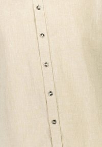 Close-up van beige stof met een verticale rij van zes zilveren metalen knopen op een gemarmerd shirt of kledingstuk.