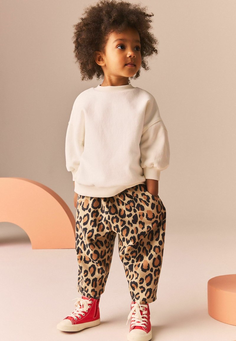 Sweatshirt blanc avec des manches bouffantes associé à un pantalon beige imprimé léopard et des baskets montantes rouges. Texture lisse, coupe décontractée.