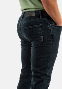 Jeans in denim scuro con una vestibilità slim, caratterizzati da un'etichetta in pelle sulla vita e accenti sottili sulle tasche posteriori.