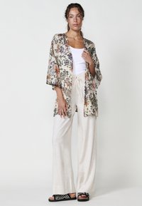 Kimono con estampado floral en una tela ligera, fondo beige, salpicaduras de color y mangas anchas, combinado con pantalones de lino color crema.