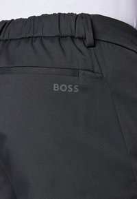Calças pretas com um acabamento texturizado, apresentando um cós elástico, um bolso traseiro e um discreto logótipo "BOSS" impresso na lateral.
