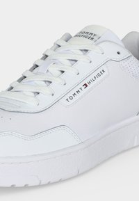 Baskets en cuir blanc avec lacets blancs, logo Tommy Hilfiger sur le côté et la languette, détails perforés près du talon.