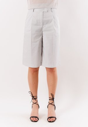 Pantaloncini grigio chiaro fino al ginocchio abbinati a sandali neri con cinturini e tacco alto su gambe nude.