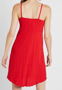 Robe rouge à rayures, sans manches, avec des bretelles fines, un corsage ajusté et un ourlet évasé. Fabriquée en tissu léger, idéale pour les temps chauds.
