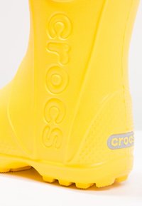 Botte de pluie en caoutchouc jaune avec une surface texturée, logo signature sur le côté et semelle à motifs.