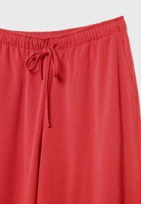 Pantalon de survêtement rouge avec une taille élastique, un cordon de serrage, et une texture douce et lisse. Dispose de poches latérales pour plus de commodité.