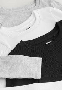 Drie lange mouwen T-shirts in zwart, wit en lichtgrijs. Elk shirt heeft een geribbelde textuur en een ronde hals, met verschillende lichte en donkere tinten.