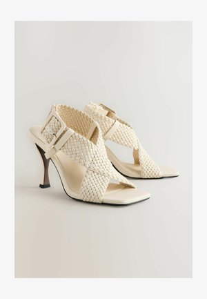 Beige högklackade sandaler med vävd överdel, öppen tådesign, korsade remmar och en slank stilettklack. Har en spänne som accent.