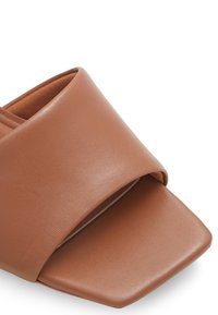 Bruna läderöppna mule-sandaler med bred rem och fyrkantig tå mot en vit bakgrund.