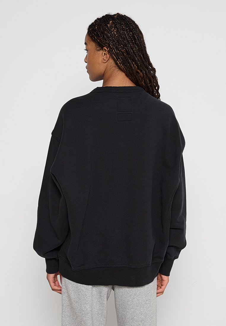 Felpa nera oversize realizzata in materiale morbido, con collo rotondo e spalle scese, dotata di un piccolo etichetta testurizzata sul retro.