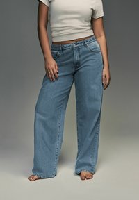 Svetlo modri široki jeans v denim materialu z visokim pasom, ki vključujejo pet žepov, zapenjanje z gumbom in zadrgo ter z bledečo teksturo.