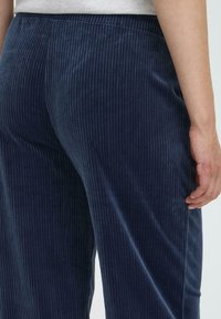 Námornícke kordové nohavice s vertikálnym brázdením, elastickým pásom a voľným strihom. Hladká textúra a jemný povrch s jemným leskom.