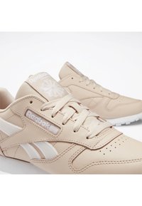 Paire de baskets en cuir beige Reebok avec des bandes blanches sur les côtés, des lacets et des logos, présentée sur un fond blanc.