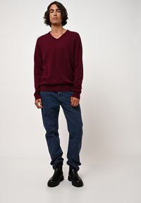 Maglione bordeaux a scollatura a V con una consistenza morbida, abbinato a jeans in denim blu e stivaletti neri lucidi. Design semplice, vestibilità rilassata.