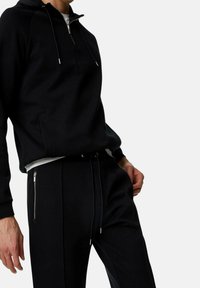 Svart träningssats med en zip hoodie och tapered byxor. Mjuk tyg, dragsnören och zipfickor ger funktionalitet till designen.