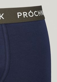 Granatowe bokserki o gładkiej fakturze, z zielonym elastycznym pasem z napisem "PRÓCHNIK" w białej literze.