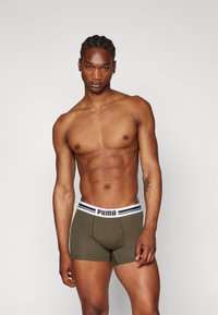 Khaki bokserice z belim pasom, okrašene s črnimi črtami in logotipom 'PUMA'. Gladek material z oblikovanim dizajnom.