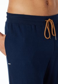 Marineblauwe geribbelde sweatpants met een drawstring in een contrasterend lichtbruin, voorzien van zijzakken en een zachte textuur.