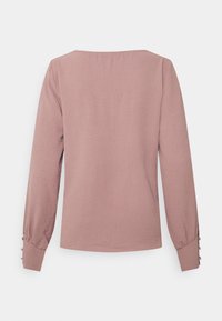 Långärmad rosa blus med fyrkantig halsringning, strukturerad tyg och knäppte manschetter. Enkel design utan mönster eller accenter.