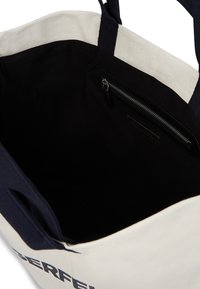 Drobėse pagaminta rankinė su kreminiu išoriniu paviršiumi ir tamsiai mėlynomis detalėmis. Vidaus dalis juoda su užtrauktuku, skirtu saugiajai laikymui.