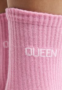 Calze rosa a costine con texture lavorata a maglia, bordo elastico e la parola "QUEEN" in bianco sul lato.