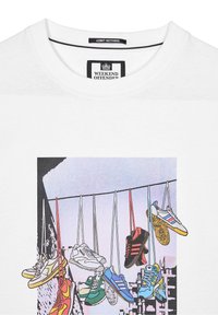 Hvid T-shirt med grafisk print af hængende sneakers i forskellige farver og design, med teksten "ADMIT NOTHING" og mærkeetiket.